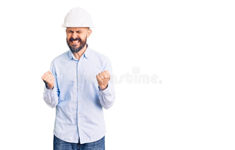 戴着建筑师硬套的年轻帅哥做赢家手势时非常高兴和兴奋，双臂高高微笑、尖叫 免版税库存照片