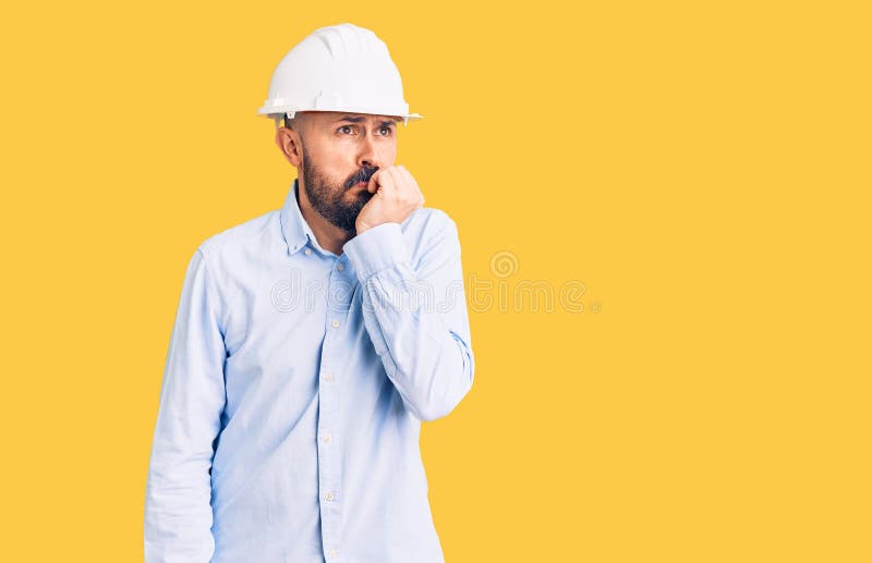 戴着建筑师硬帽的年轻帅气男人，手咬口指甲显得紧张 库存照片