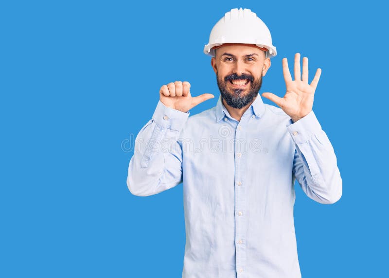 戴着建筑师精装帽的年轻帅哥一边微笑着自信而快乐地指着六指 免版税图库摄影