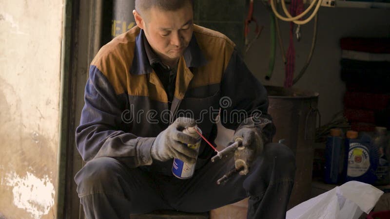 戴着手套和工作服的亚洲人,正在修理车库里汽车的一个备用部分 影视素材