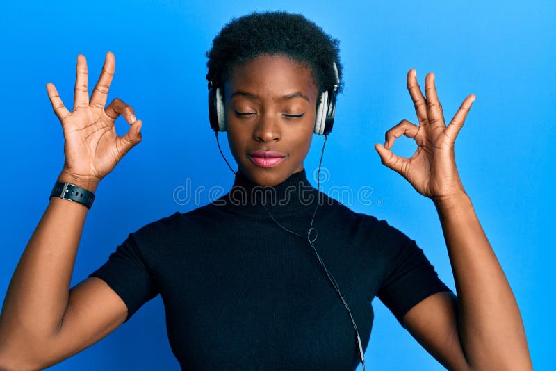 戴耳机听音乐的非洲裔年轻女孩放松，微笑着闭上眼睛做冥想手势 免版税库存照片