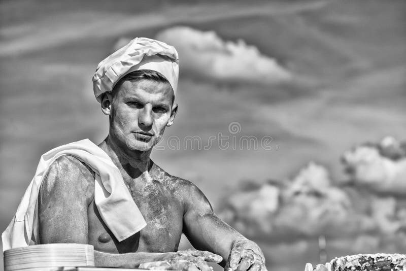 Man muscular baker or cook covered with flour working outdoor, sky on background. Bakery concept. Man with muscular sexy torso works as chef cook. Baker at working surface covered with flour. Man muscular baker or cook covered with flour working outdoor, sky on background. Bakery concept. Man with muscular sexy torso works as chef cook. Baker at working surface covered with flour.