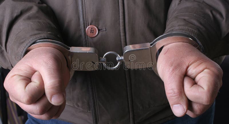 Detail of the hands of a arrested man, with handcuffs. Detail of the hands of a arrested man, with handcuffs