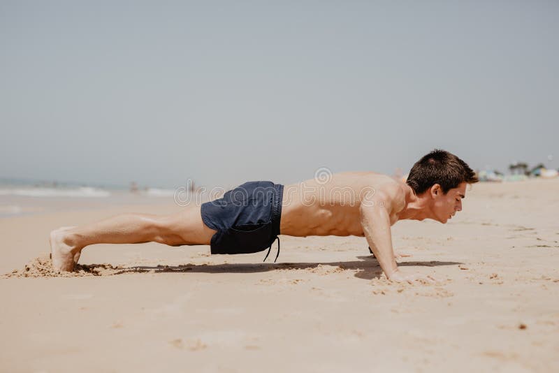 执行俯卧撑微笑的健身人愉快 在海滩的男性健身设计交叉培训