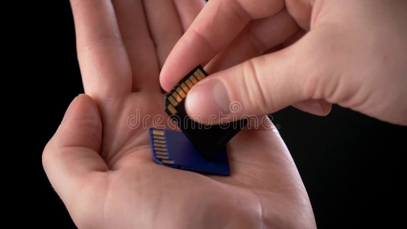 拿着存储卡SD卡片-安全数字式卡片的男性手用于摄象机和计算机在蓝色颜色作为a