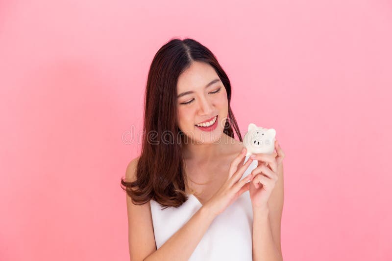 拿着存钱罐的年轻亚裔妇女画象,愉快和激动在自己的挽救被隔绝在生动的桃红色背景 库存图片 拿着存钱罐的年轻亚裔妇女画象,愉快和激动在自己的挽救被隔绝在生动的桃红色背景 库存图片