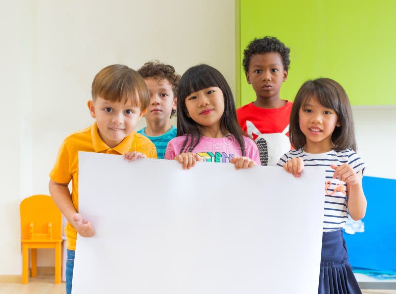 拿着空白的海报的变化孩子在教室在kinderga 库存照片