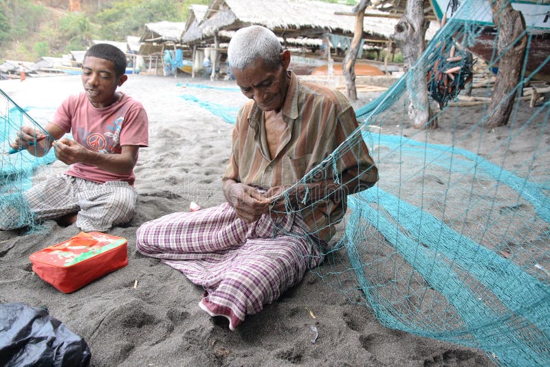 An old whaler from Lamalera village repairs fishing nets on a beach. Villagers of Lamalera on Lembata island, East Indonesia, are the last people on Earth who regularly hunt whales with hand harpoons. They use non-motor wooden boats to chase a whale and then a whaler throws bamboo harpoons from the tip of its boat. This way of hunting is dangerous, sometimes boats sink or are pulled by whales for miles (and days) before a whale dies. Lamalera villagers only occasionally use money, most often they exchange directly goods with other villages and in this way they get other types of food in exchange of fish and whale meat. Between fishing and hunting, whalers spend their time on a beach making tools and repairing their boats. An old whaler from Lamalera village repairs fishing nets on a beach. Villagers of Lamalera on Lembata island, East Indonesia, are the last people on Earth who regularly hunt whales with hand harpoons. They use non-motor wooden boats to chase a whale and then a whaler throws bamboo harpoons from the tip of its boat. This way of hunting is dangerous, sometimes boats sink or are pulled by whales for miles (and days) before a whale dies. Lamalera villagers only occasionally use money, most often they exchange directly goods with other villages and in this way they get other types of food in exchange of fish and whale meat. Between fishing and hunting, whalers spend their time on a beach making tools and repairing their boats.