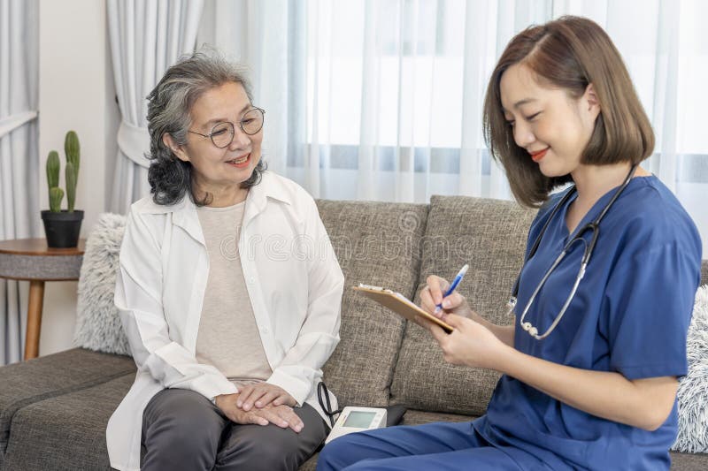 接受健康面试的高级女护士带纸夹板记录病人数据 免版税图库摄影
