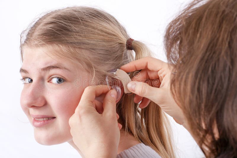 Doctor inserting a hearing aid into a young girl's ear in front of a white background. Doctor inserting a hearing aid into a young girl's ear in front of a white background