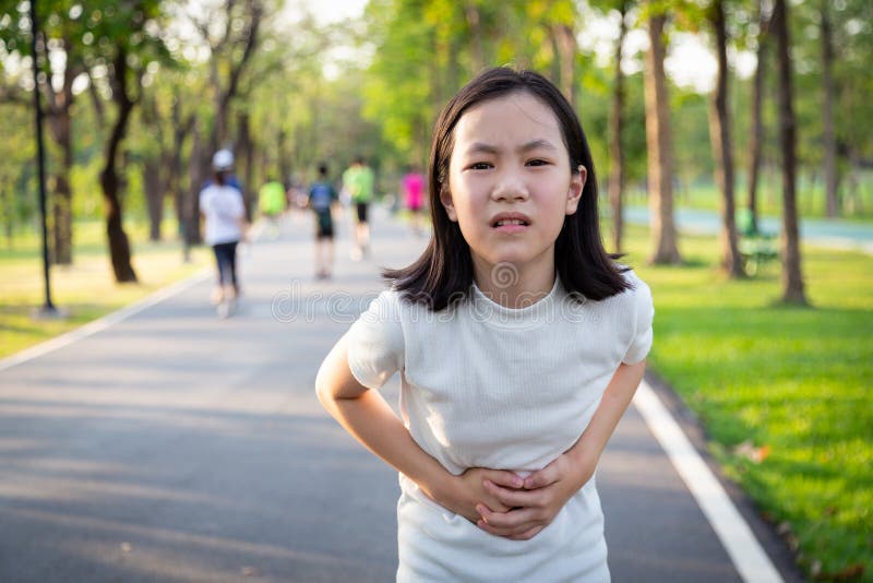 握她的在腹部的不快乐的亚裔矮小的逗人喜爱的女孩手,遭受胃痛,绞痛在跑,锻炼以后在室外公园, 免版税图库摄影 握她的在腹部的不快乐的亚裔矮小的逗人喜爱的女孩手,遭受胃痛,绞痛在跑,锻炼以后在室外公园, 免版税图库摄影