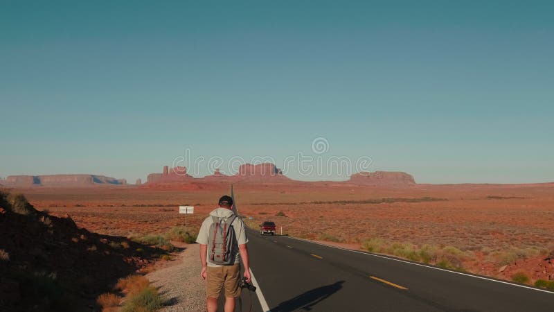 摄像机在亚利桑那州砂岩沙漠中拖着背包和摄像头的顺风徒步旅行者