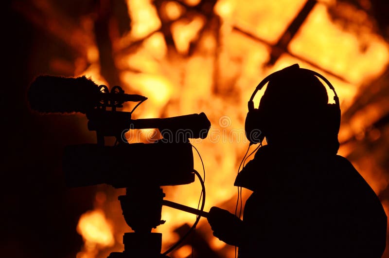 A news reporter, journalist cameraman filming a building that is full of leaping hot flames and burning to the ground. No people were hurt in this fire. A news reporter, journalist cameraman filming a building that is full of leaping hot flames and burning to the ground. No people were hurt in this fire.