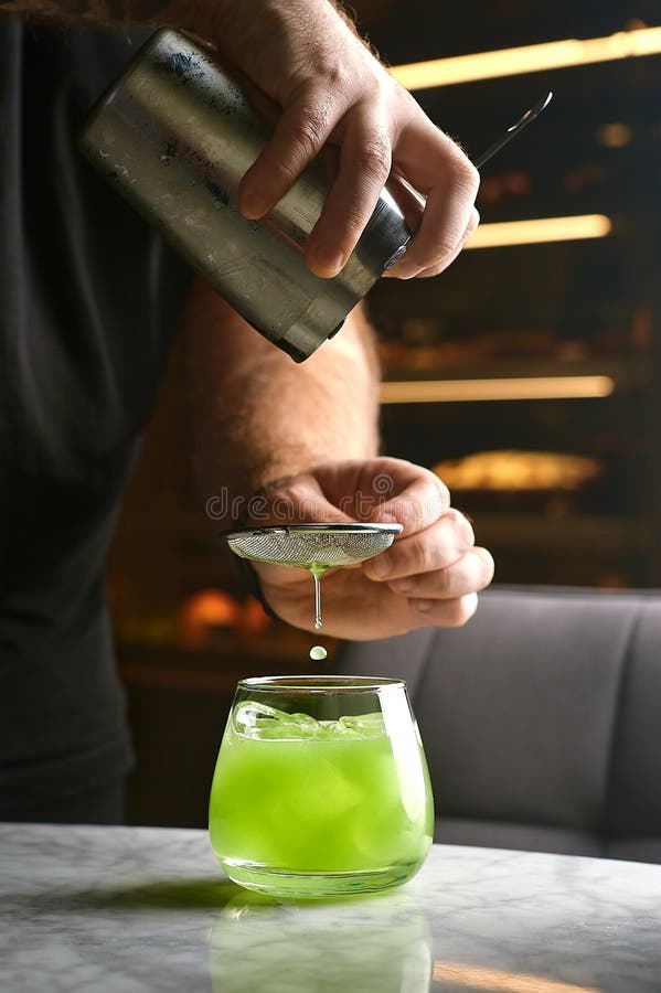 摇瓶玻璃杯中酒保手浇巴西勒鸡尾酒的特写. 巴尔曼准备经典现代罗勒 免版税图库摄影