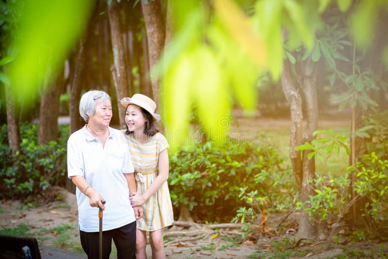 支持资深妇女用拐棍、愉快的微笑的祖母和孙女的亚裔女孩在公园,年长 库存照片 支持资深妇女用拐棍、愉快的微笑的祖母和孙女的亚裔女孩在公园,年长 库存照片