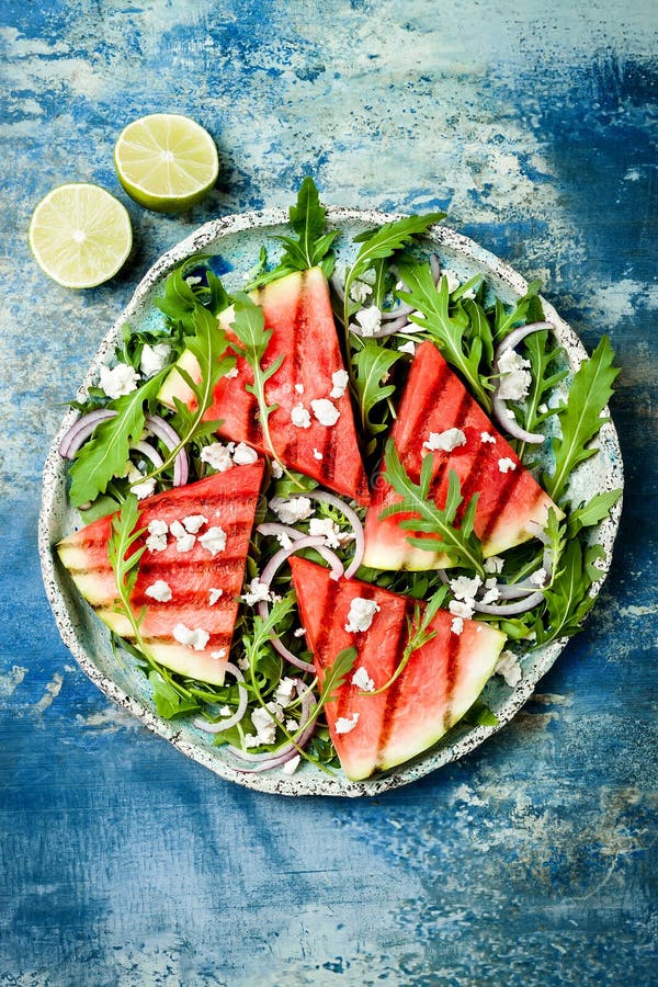 Fresh summer grilled watermelon salad with feta cheese, arugula, onions on blue background. Fresh summer grilled watermelon salad with feta cheese, arugula, onions on blue background