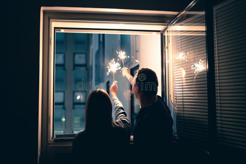 新年窗口火花. 一对夫妇在家庆祝. 与家人共度晚会. 夜里闪闪发光. 图库摄影
