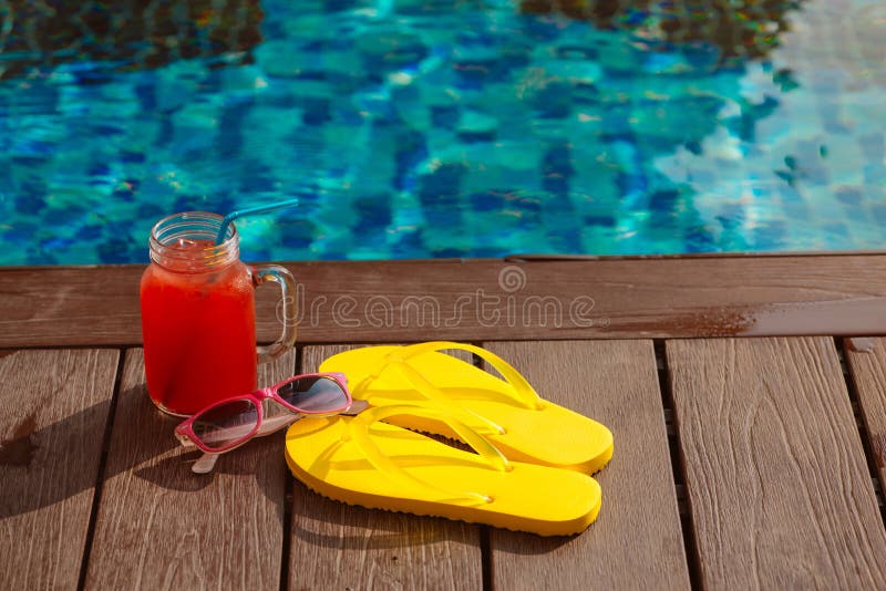 Fresh glass of water-melon smoothie drink with sunglasses, straw hat and slippers on border of a swimming pool - holiday tropical concept. Fresh glass of water-melon smoothie drink with sunglasses, straw hat and slippers on border of a swimming pool - holiday tropical concept