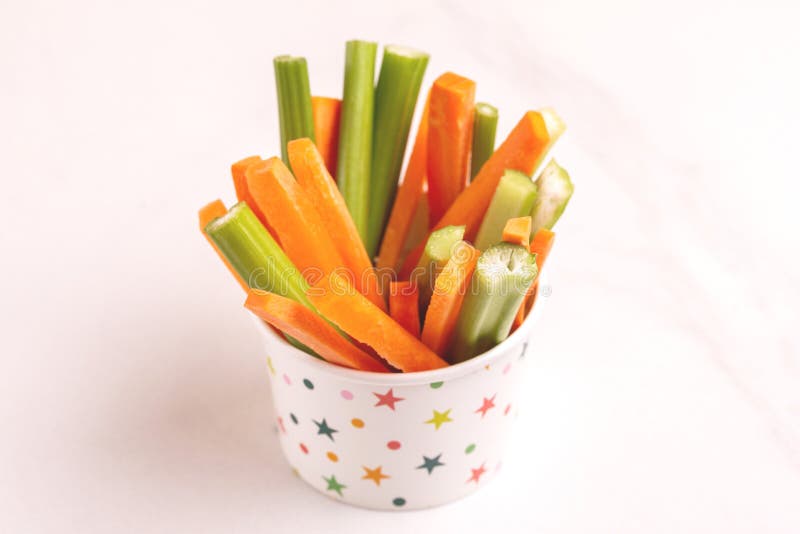 Fresh carrots and celery sticks in paper cup on light marble background. Healthy food concept. Copy space. Fresh carrots and celery sticks in paper cup on light marble background. Healthy food concept. Copy space