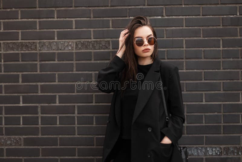 时尚模特、艳丽的年轻女性，戴着酷圆的墨镜，穿着时髦的黑色休闲夹克，接近现代时尚 免版税库存图片