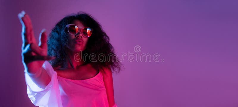 Fashion young african girl black woman wear stylish pink glasses dance look at camera shoot hand gun  on party disco purple studio background, banner for website design, portrait, copy space. Fashion young african girl black woman wear stylish pink glasses dance look at camera shoot hand gun  on party disco purple studio background, banner for website design, portrait, copy space