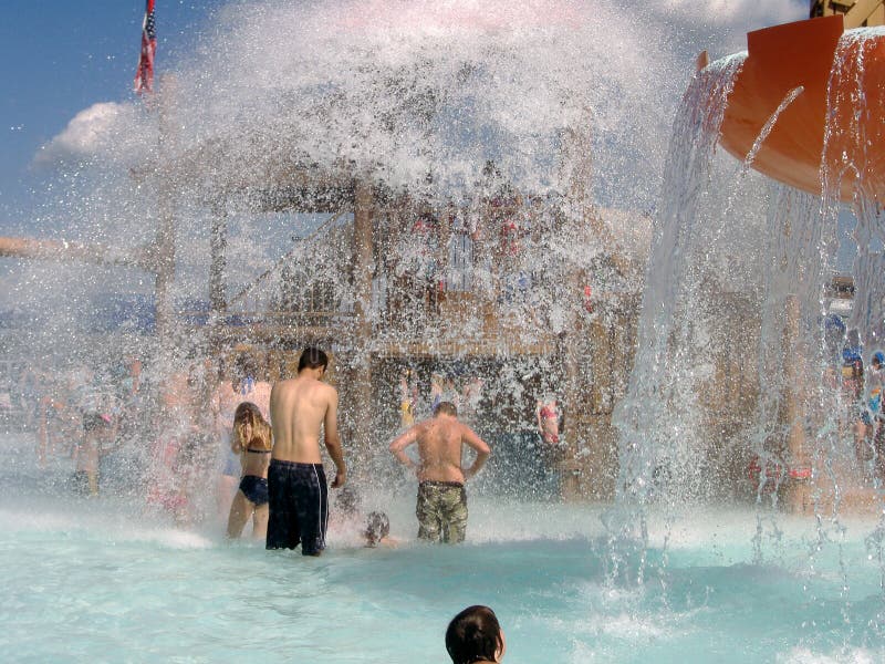 Boys & girls of all ages get splashed by the plume from the giant water bucket above at a modern community water park. Boys & girls of all ages get splashed by the plume from the giant water bucket above at a modern community water park.