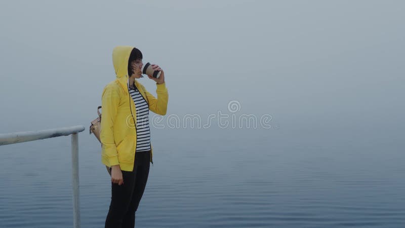 昏昏欲睡的女人喝咖啡，雾蒙蒙的早晨在水上码头等船 股票视频