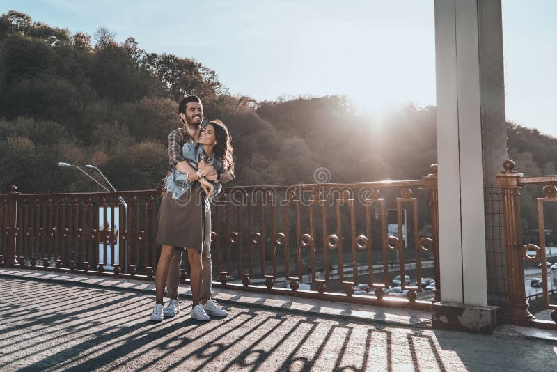 Full length of beautiful handsome men embracing young attractive women while standing on the bridge outdoors. Full length of beautiful handsome men embracing young attractive women while standing on the bridge outdoors