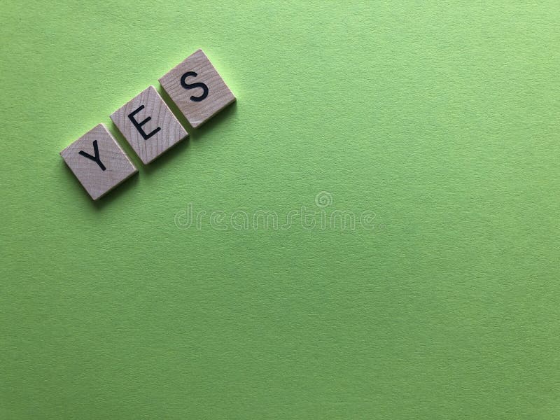 The word Yes,  spelt out in wood letters on a plain green background with copy space. The word Yes,  spelt out in wood letters on a plain green background with copy space.