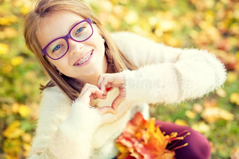 戴显示心脏用手的括号和眼镜的微笑的小女孩 Autum时间 免版税库存图片