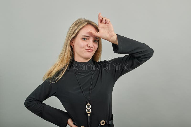 Showing loser sign, displaying dud gesture, alpha. Two fingers 2, disgust on face, negative human emotion facial expression. Young attractive woman, dressed black sweater with green eyes, blonde hair. Showing loser sign, displaying dud gesture, alpha. Two fingers 2, disgust on face, negative human emotion facial expression. Young attractive woman, dressed black sweater with green eyes, blonde hair