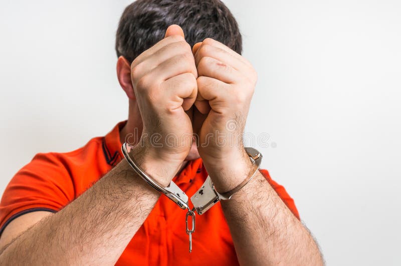 Arrested man in handcuffs hidden his face in front of camera. Arrested man in handcuffs hidden his face in front of camera