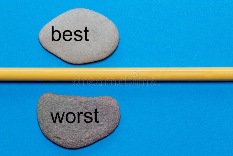 The words best and worst are written on natural smooth stones separated by a yellow pencil. The background is isolated in blue and has a lot of space . The words best and worst are written on natural smooth stones separated by a yellow pencil. The background is isolated in blue and has a lot of space .