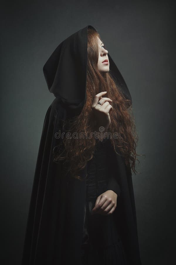 Dark portrait of a beautiful red haired woman with black robe . Halloween and fantasy concept. Dark portrait of a beautiful red haired woman with black robe . Halloween and fantasy concept