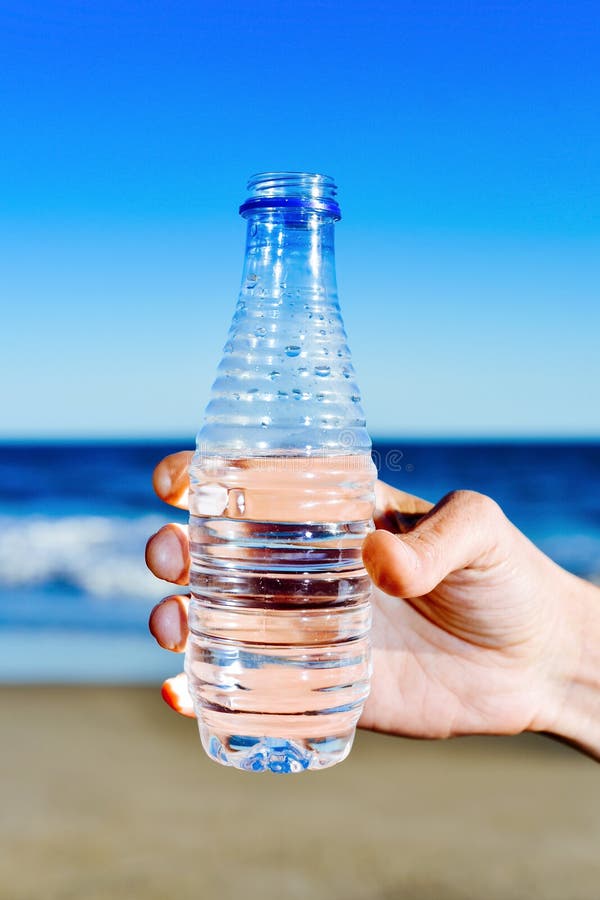 Closeup of a young man with a water bottle in his hand in front of the sea. Closeup of a young man with a water bottle in his hand in front of the sea