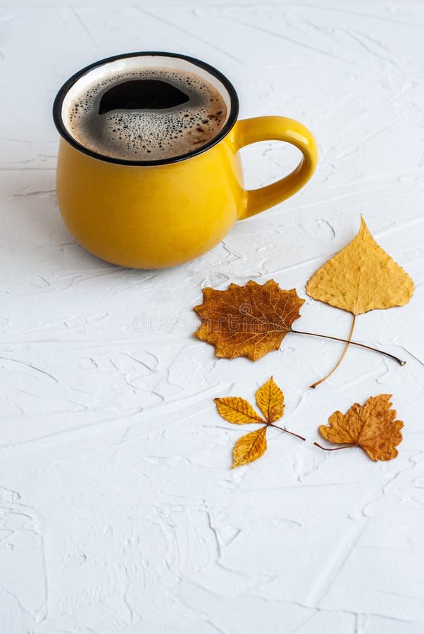 Bright yellow cup with a hot coffee drink, autumn dry leaves on a white background. Comfort, warm atmosphere, season, season. Autumn concept. Close-up. Bright yellow cup with a hot coffee drink, autumn dry leaves on a white background. Comfort, warm atmosphere, season, season. Autumn concept. Close-up