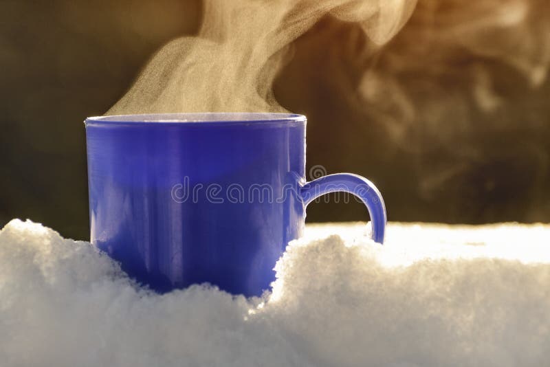 Blue mug with a steaming hot drink is standing in the snow. Winter sunny day. Blue mug with a steaming hot drink is standing in the snow. Winter sunny day.