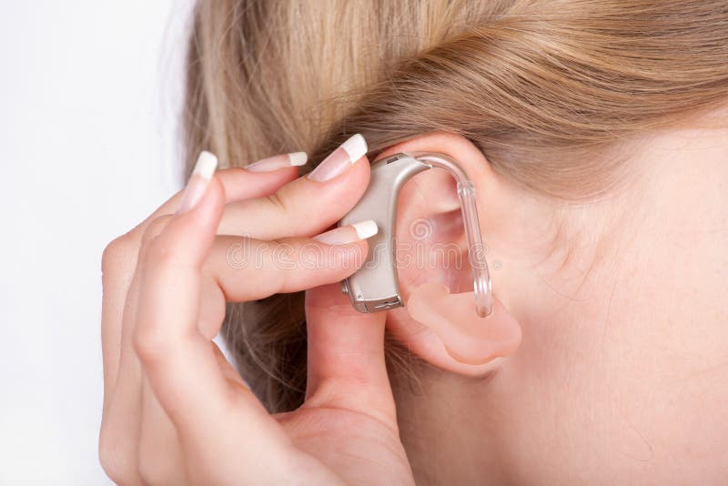 Close up of an ear of a girl with a hand inserting a hearing aid. Close up of an ear of a girl with a hand inserting a hearing aid