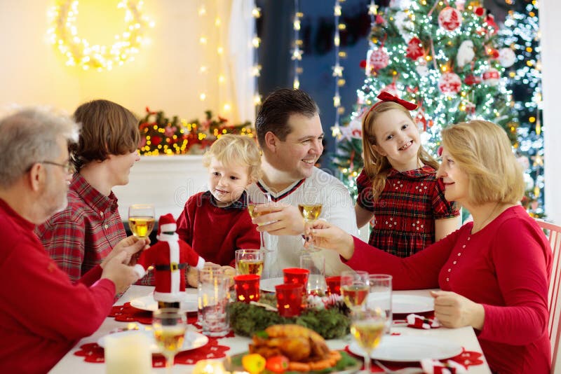 有吃圣诞晚餐的孩子的家庭在壁炉和装饰的Xmas树 父母、祖父母和孩子在欢乐膳食 库存图片