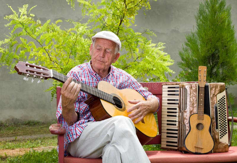 Old man playing acoustic guitar with closed eyes in his garden. Old man playing acoustic guitar with closed eyes in his garden