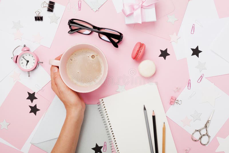 Female hand with coffee cup, macaron, office supply, gift and notebook on pastel desk top view. Fashion pink woman workplace background for blogging. Flat lay. Beautiful morning breakfast. Female hand with coffee cup, macaron, office supply, gift and notebook on pastel desk top view. Fashion pink woman workplace background for blogging. Flat lay. Beautiful morning breakfast.