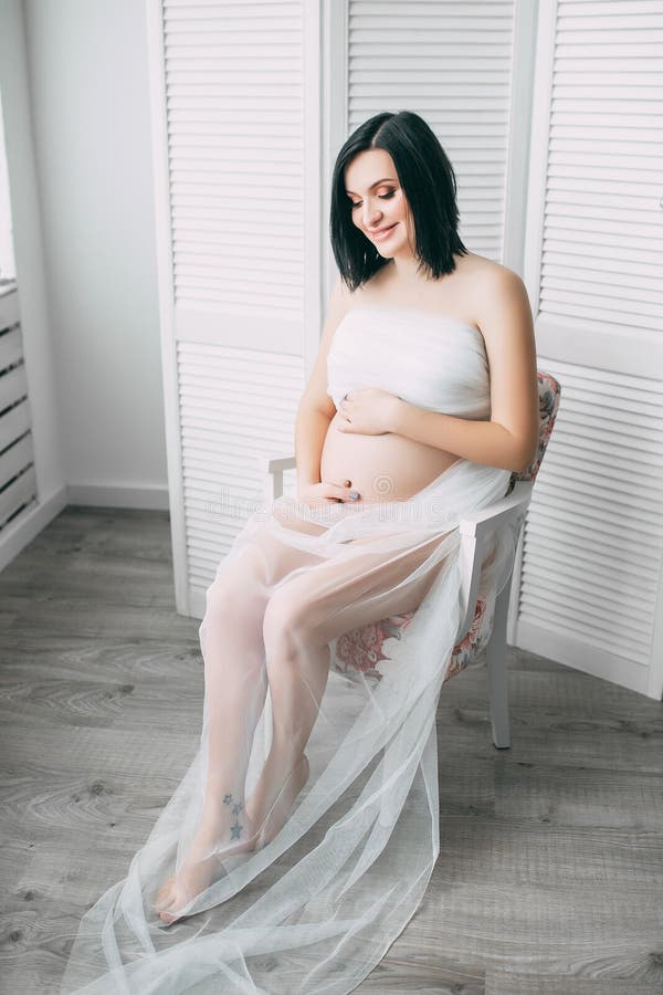 有大腹部的愉快的美丽的怀孕的白种人妇女在白色内衣在卧室，未来parrents，等待