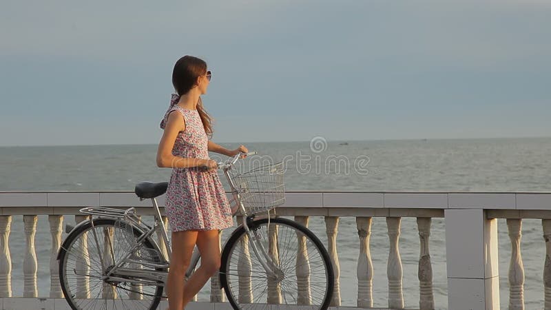 有她的自行车的美丽的女孩在海滩附近的堤防