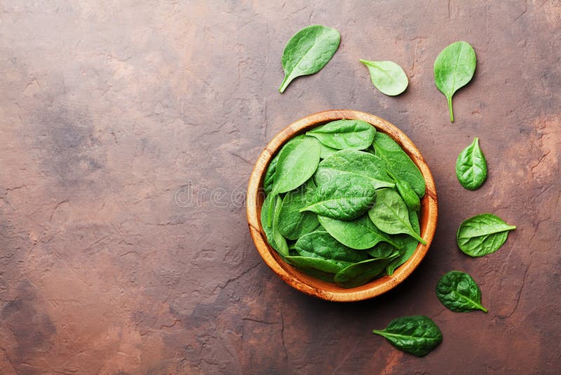 Organic food. Baby spinach leaves in wooden bowl on rustic stone table top view. Copy space. Organic food. Baby spinach leaves in wooden bowl on rustic stone table top view. Copy space.