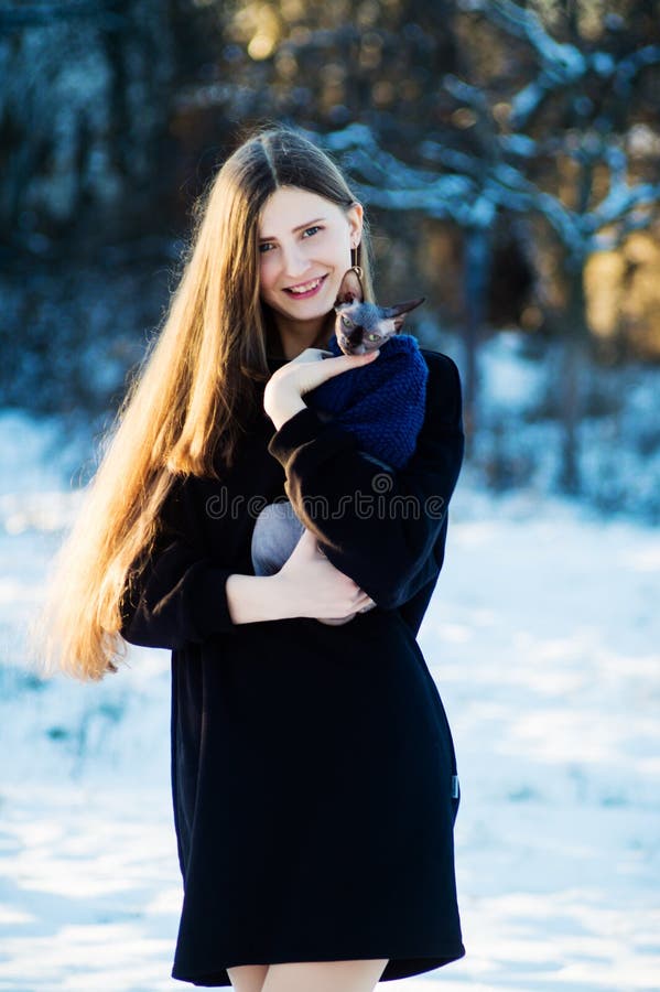 有猫品种唐狮身人面象的美丽的女孩在她的手上在冬天在公园