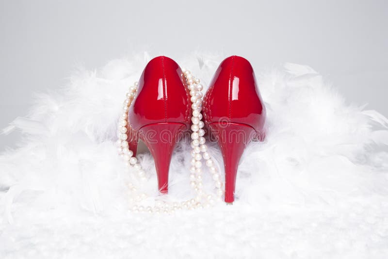 A pair of sexy, red patent leather pumps sit atop a white fur surface with a white background; pearls and a white boa surround the shoes. A pair of sexy, red patent leather pumps sit atop a white fur surface with a white background; pearls and a white boa surround the shoes
