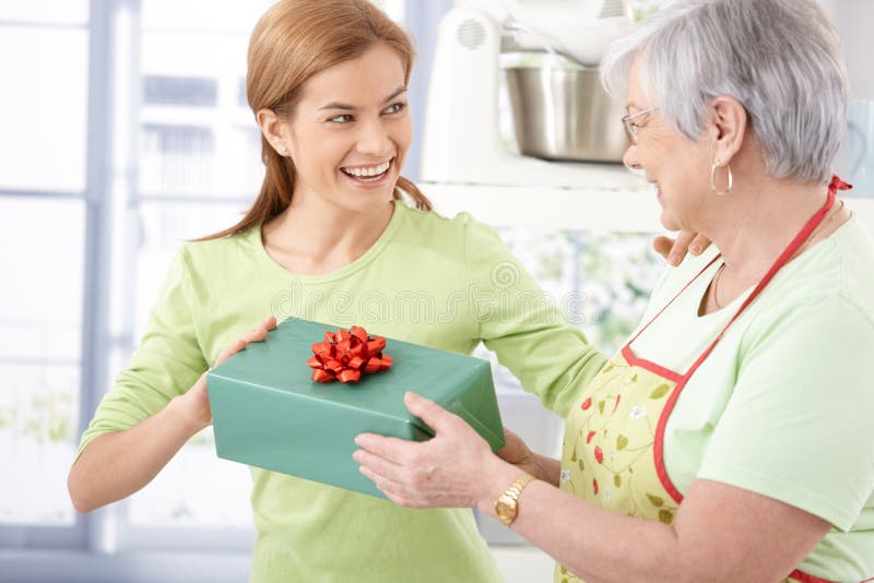 Happy young female presenting her mother with wrapped gift, both smiling. Happy young female presenting her mother with wrapped gift, both smiling.