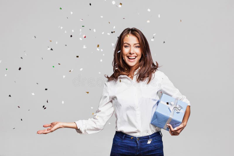 Beautiful happy woman with gift box at celebration party with confetti falling everywhere on her. Birthday or New Year eve celebrating concept. Beautiful happy woman with gift box at celebration party with confetti falling everywhere on her. Birthday or New Year eve celebrating concept