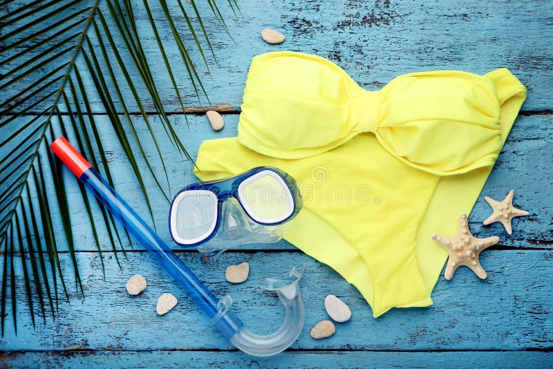 Swimsuit with green palm leaf and diving mask on blue wooden table. Swimsuit with green palm leaf and diving mask on blue wooden table