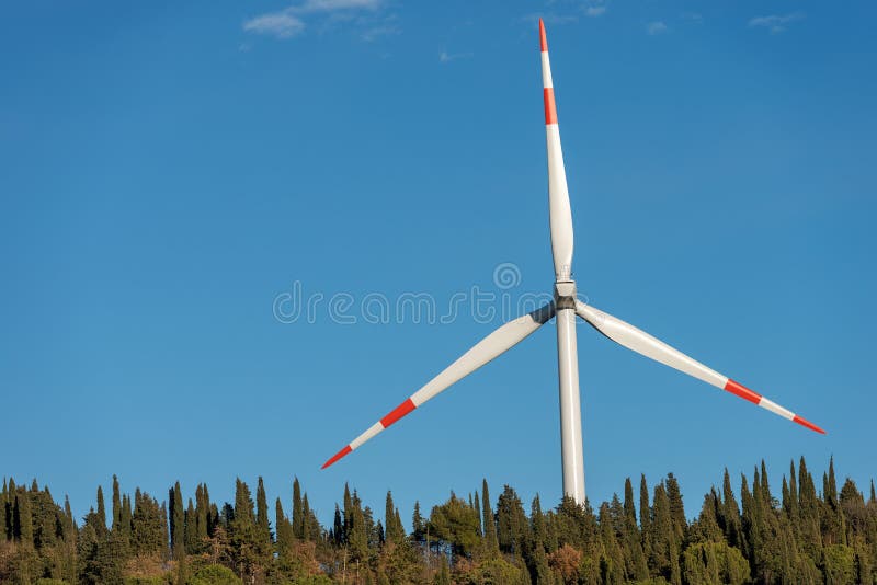 White and red wind turbine on a clear blue sky with trees. Sustainable resource. White and red wind turbine on a clear blue sky with trees. Sustainable resource